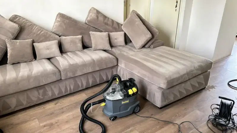 Hoekbank van velours in een woonkamer, net gereinigd, met de extractiemachine ernaast