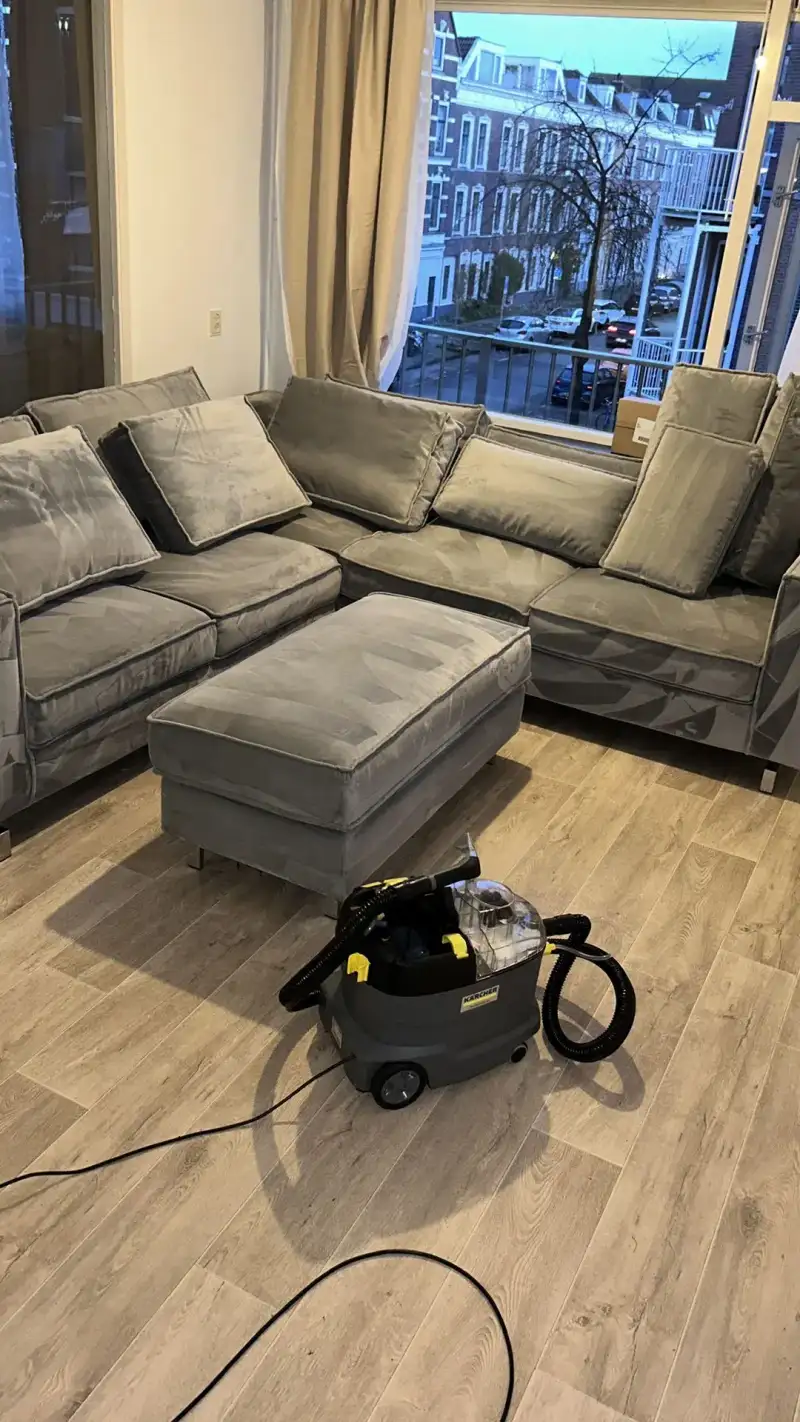 Hoekbank en poef van velours in een woonkamer, met de extractiemachine op de vloer