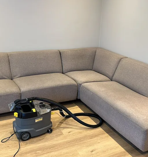 Grijze hoekbank na de dieptereiniging, met de extractiemachine ervoor op de houten vloer