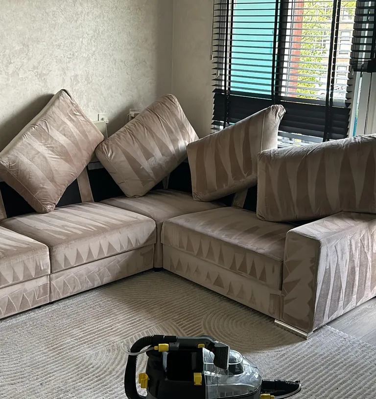 Hoekbank en vloerkleed in een woonkamer na de reiniging, de extractiemachine staat nog op het kleed
